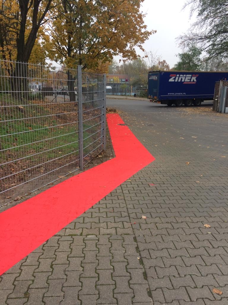 Rote Fahrradwegmarkierung auf einer Pflasterfläche neben einem Gewerbegelände